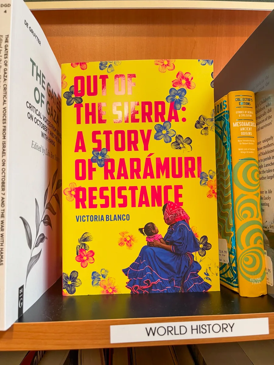A yellow book on a bookshelf in a store that says Out of the Sierra with a raramuri woman on the cover.