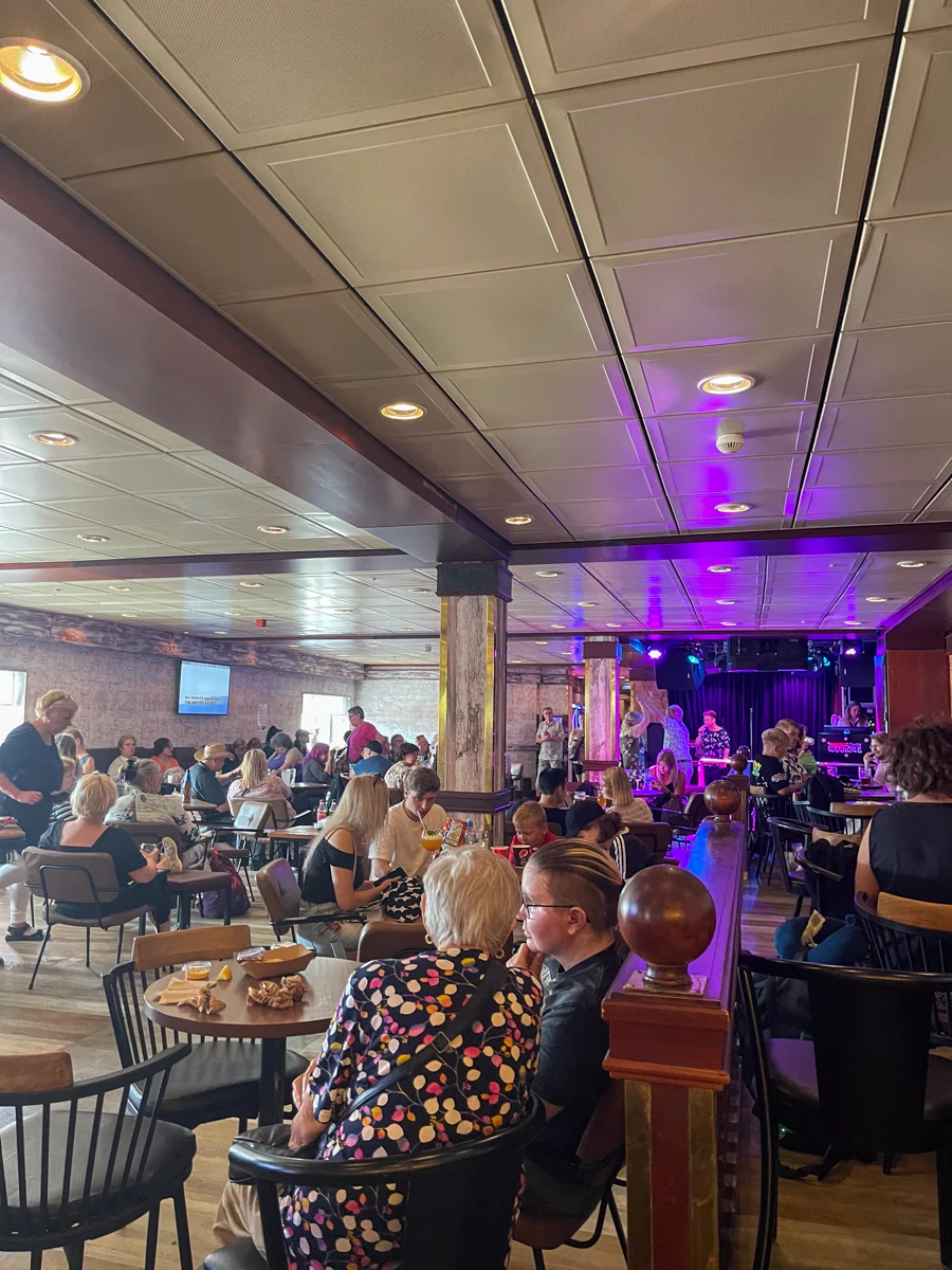 people seated in a bar with purple lights over a stage where people are signing on a small stage.