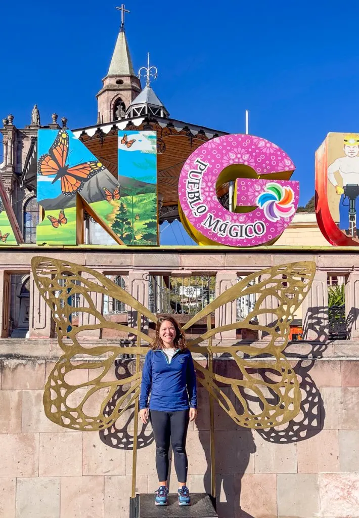 woman standing in front of a colorful sign with butterfly wings behind her.