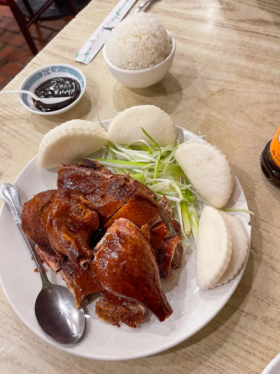 peking duck on a plate with bao buns and dipping sauce.
