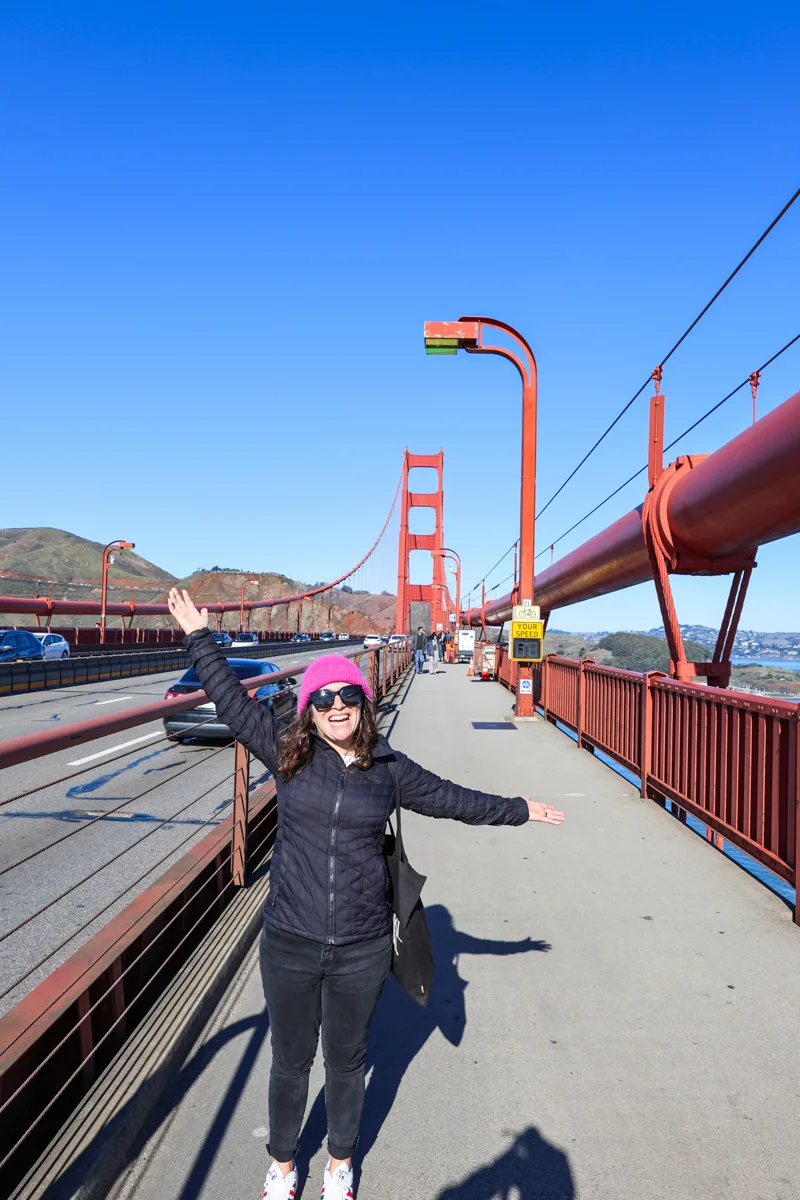 woman standing on the golden gate bridge with a bright pink winter had and coat.