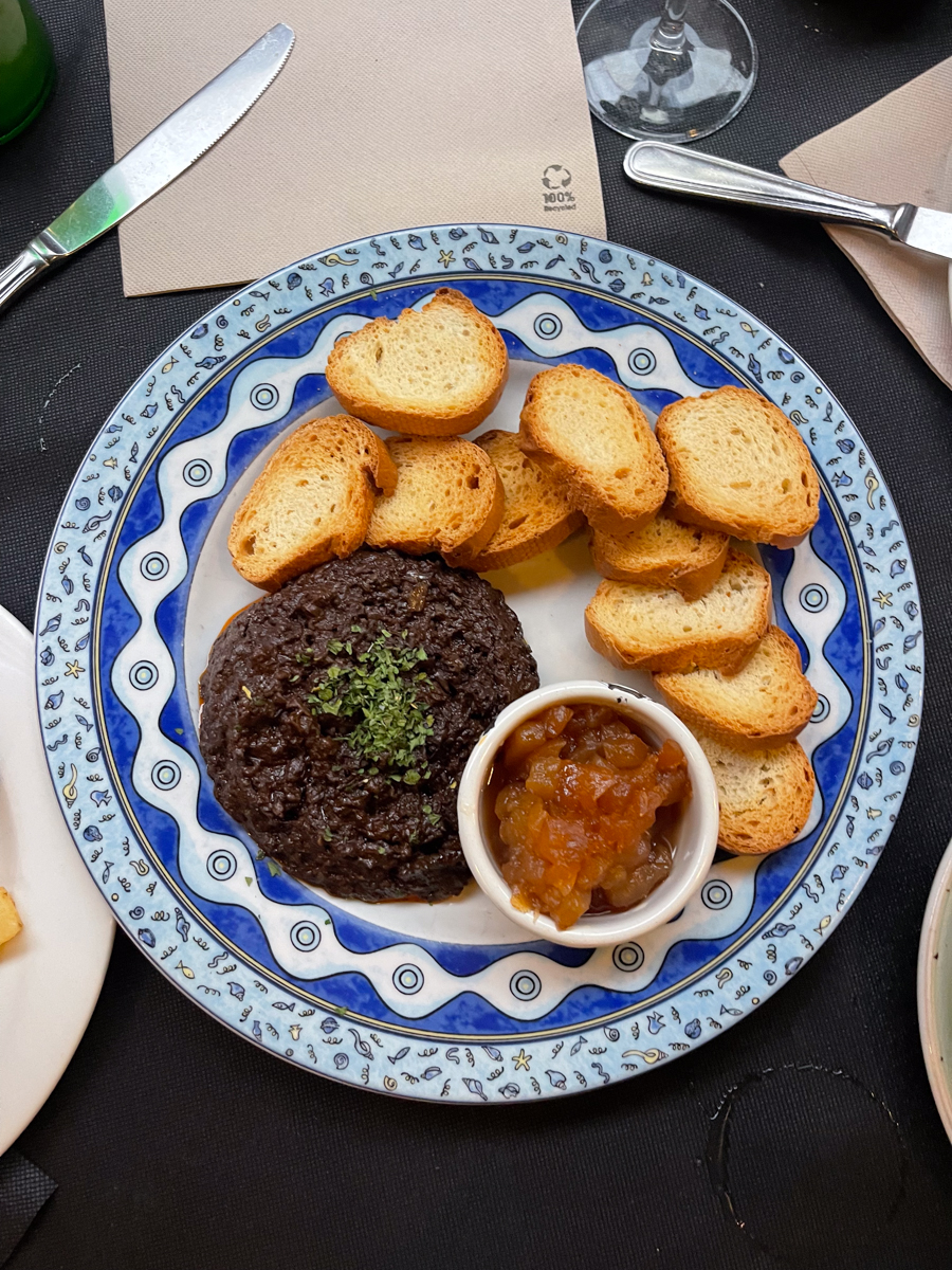 a plate of morcilla with small pieces of toast and a dip in a white cup on the side.
