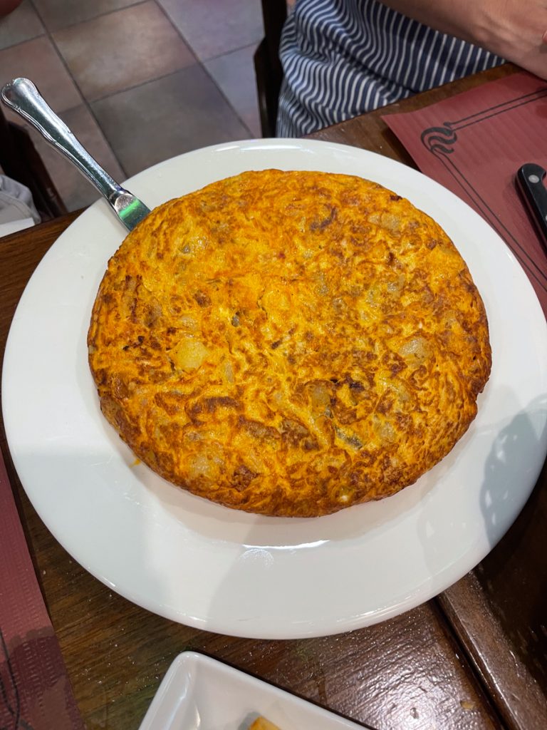 Spanish tortilla on a white plate with a butter knife wedged underneath it.