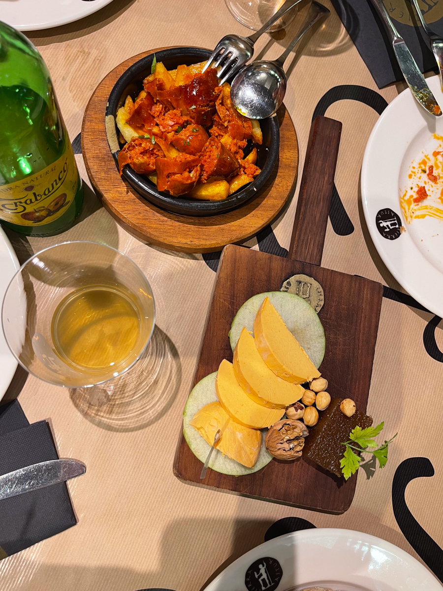 table shot from above with a glass of cider to the left, a black skillet filled with chorizo and fries at the top and a tablet of yellow triangles of cheese on the bottom.
