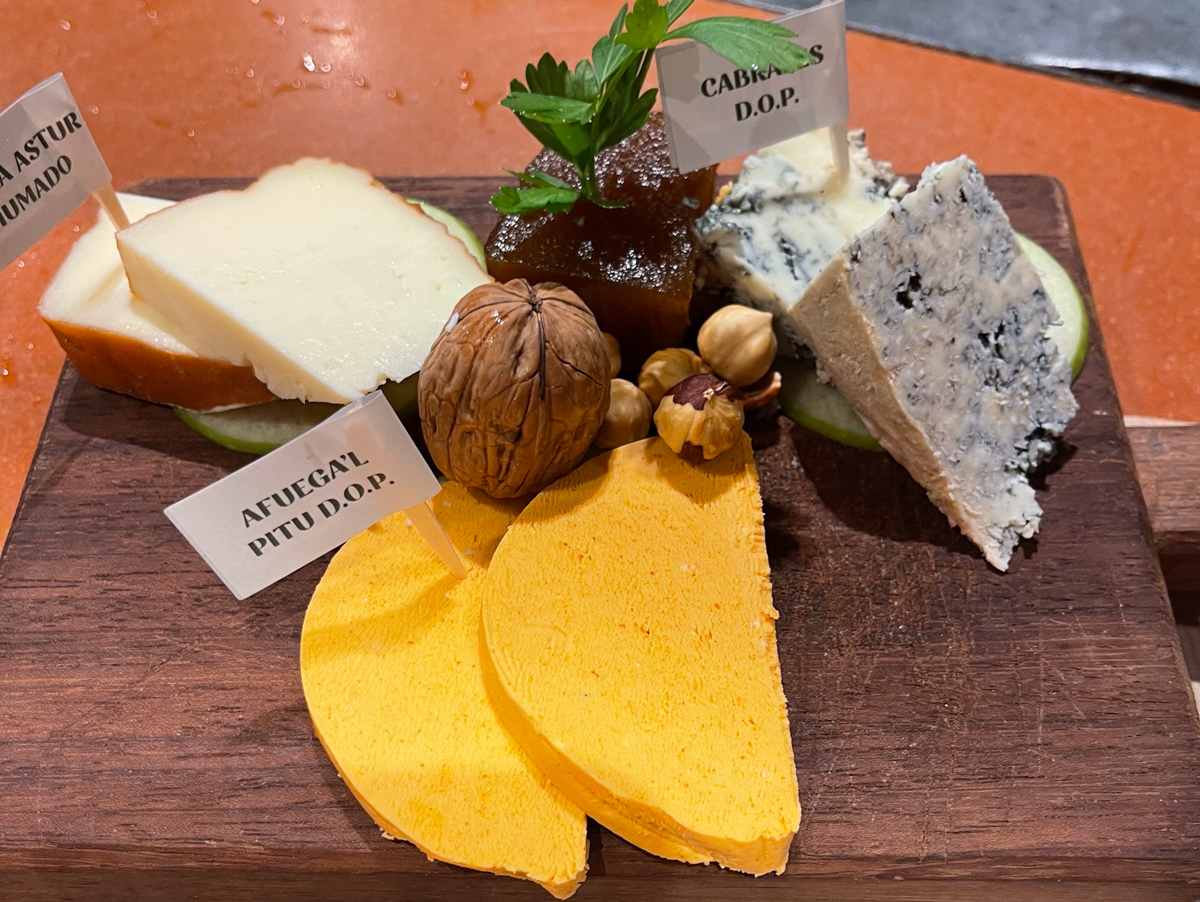 a small chopping board topped with three different types of cheese and small flags sticking out of each section saying the name of the cheese on it.