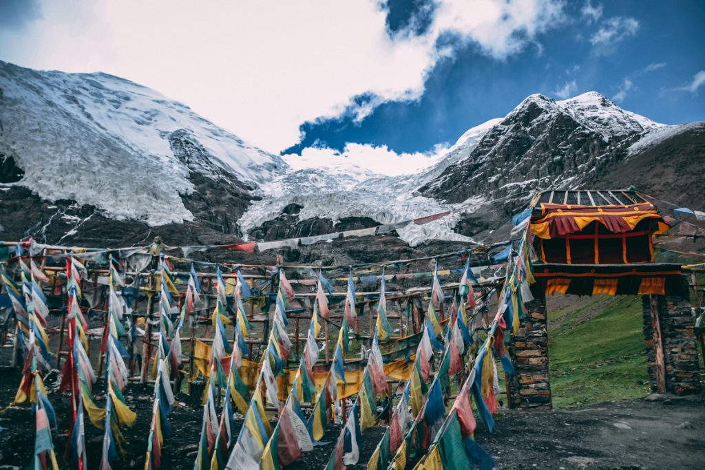everest base camp on the tibet side with blue and white cloud skies above and snow capped mountains in the background with tibetan prayer flags fluttering in the wind in the foreground.